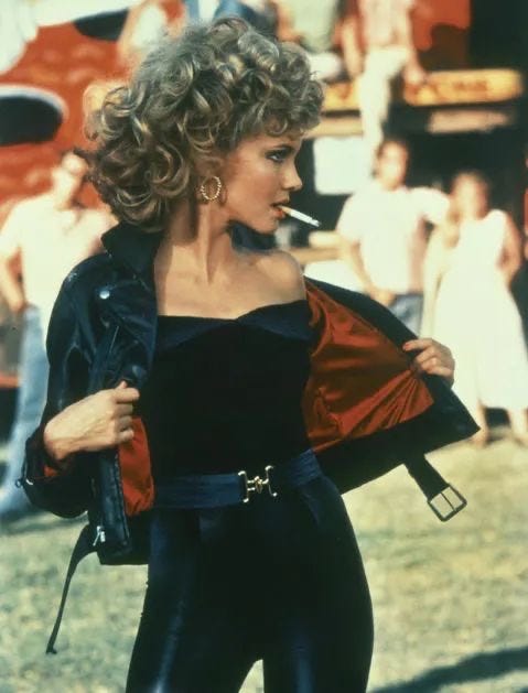 Miss Sandy (from Grease) after she changes into a stunning bad girl. Blonde woman with big curls, red lipstick, leather everything and a cigarette seducing a 47year old actor pretending to be 17