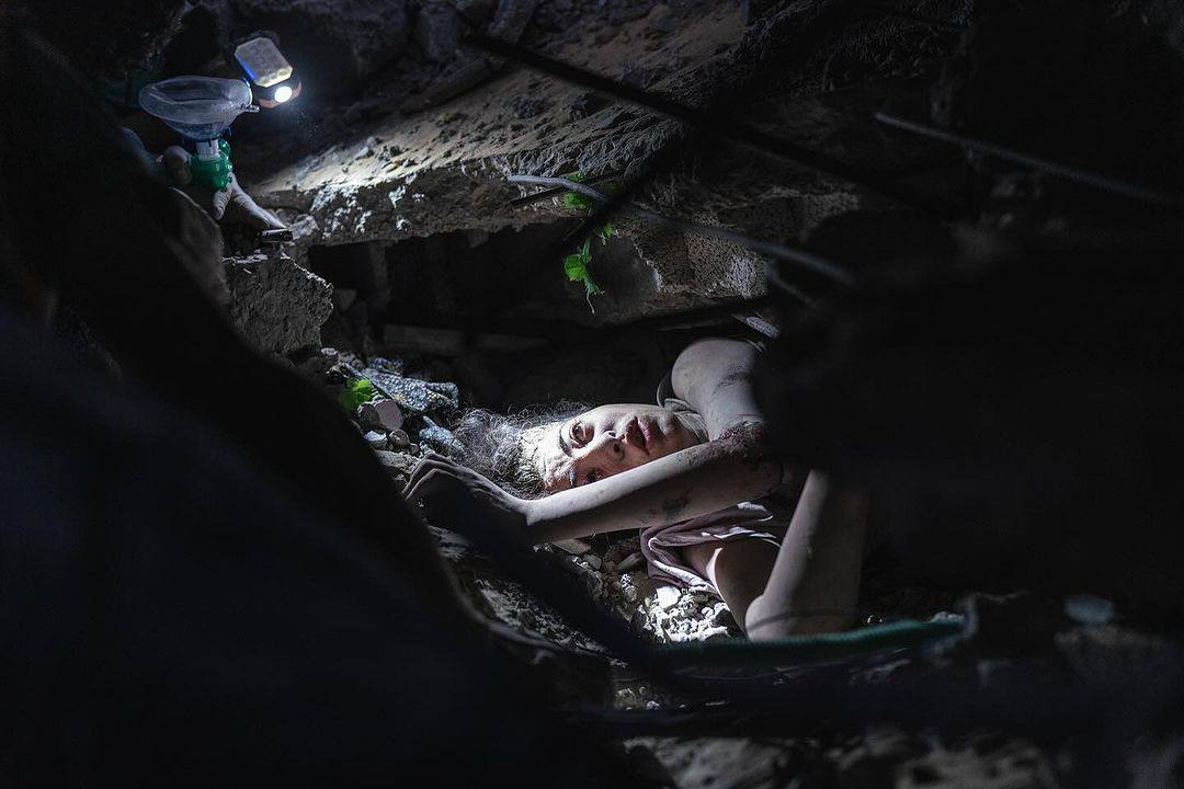 A young girl is photographed stuck under the rubble of her house after being bombed by the israeli warplanes. 31 October 2023. she is covered in dirt and dust and looks up to the search light that illuminates her, terrified.