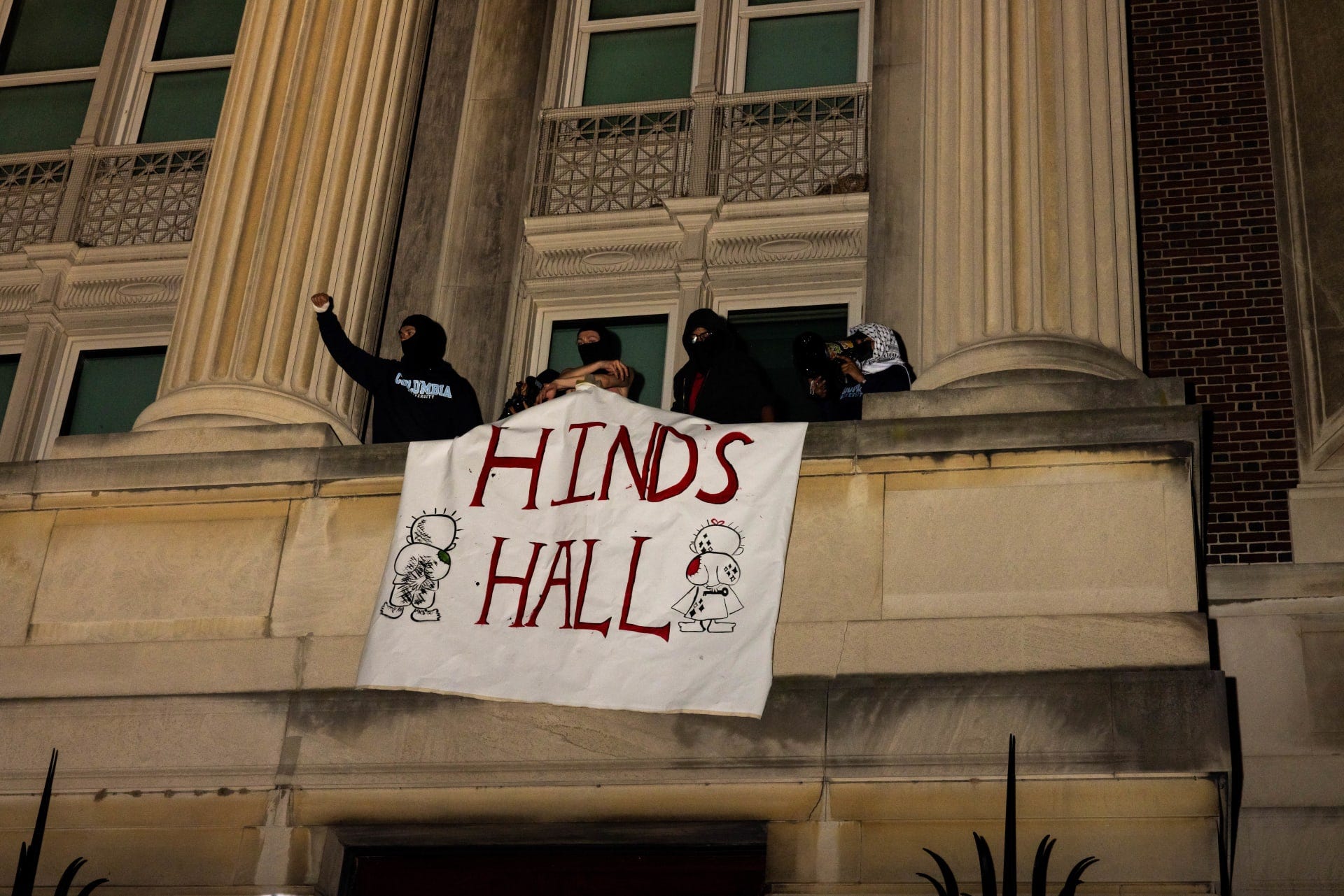 أسموها "قاعة هند".. طلاب متضامنون مع الفلسطينيين يغلقون مدخل "قاعة …Four students with their faces covered stand on a veranda between two columns. They hold a banner that reads HIND’S HALL in bold, red typeface. These students occupy Hamilton Hall on Columbia University in protest and in remembrance of Hind Rajab, martyred by the Israeli regime at age six.